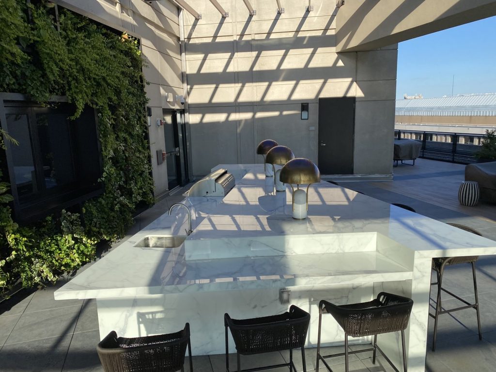 Rooftop outdoor kitchen island under pergola with raised marble bar top