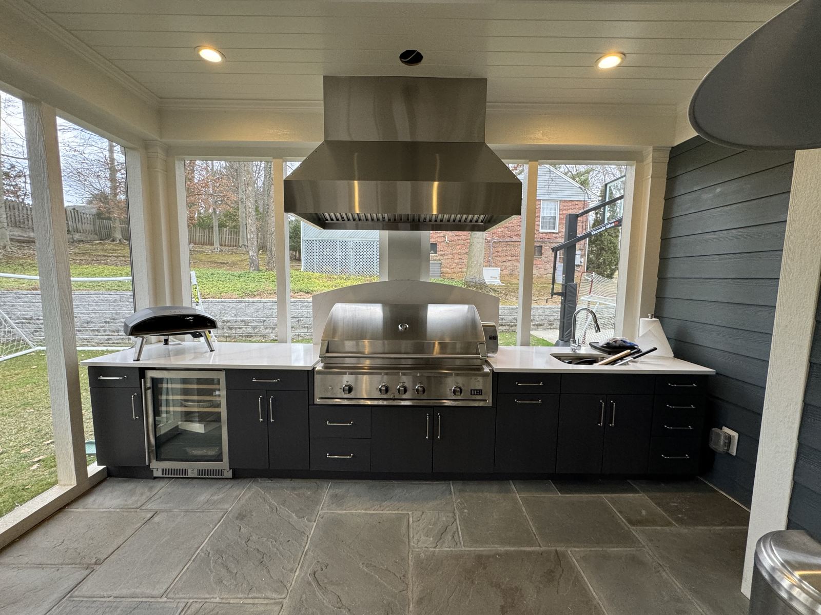 Screened porch outdoor kitchen with stainless ventilation hood and weather-rated cabinetry by SMFW